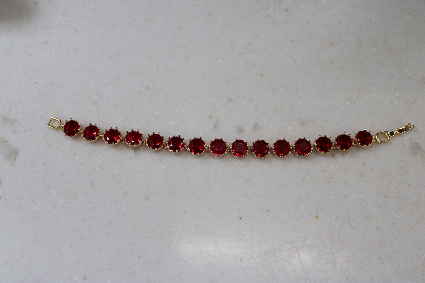 Gold bracelet with red gemstones on a light gray surface